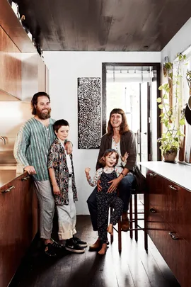 Family of four smiling in a modern kitchen with wooden cabinets and plants by the window.