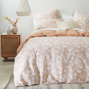 Floral patterned bed with beige and white tones, matching pillows, wooden nightstand, and decorative vases.