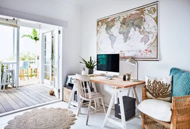 Cozy home office with a desk, computer, world map, and open doors leading to a balcony with seating.