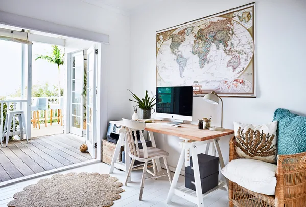 Cozy home office with a desk, computer, world map, and open doors leading to a balcony with seating.