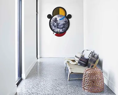 A modern room with a circular abstract artwork on the wall, bench with cushions, and a wicker basket on the floor.
