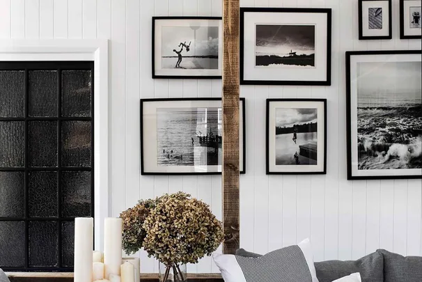 Gallery wall with black-and-white photos, a rustic wood beam, dried flowers in a vase, and white candles.