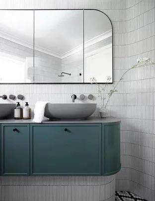Modern bathroom with teal cabinet, round basin, large wall mirror, and small vases on a checkered floor.