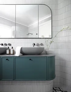 Modern bathroom with teal cabinet, round basin, large wall mirror, and small vases on a checkered floor.