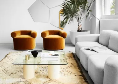 Luxurious living room with mustard velvet chairs, gray sofa, glass coffee table, geometric wall art, and a potted plant.