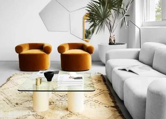 Luxurious living room with mustard velvet chairs, gray sofa, glass coffee table, geometric wall art, and a potted plant.