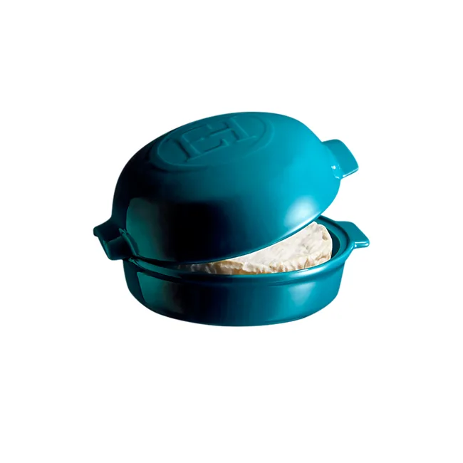 Teal ceramic cheese baker with lid slightly open, revealing a round white cheese inside.