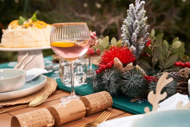 Festive table setting with a pink cocktail, cake, and holiday decorations, including greenery and red flowers.