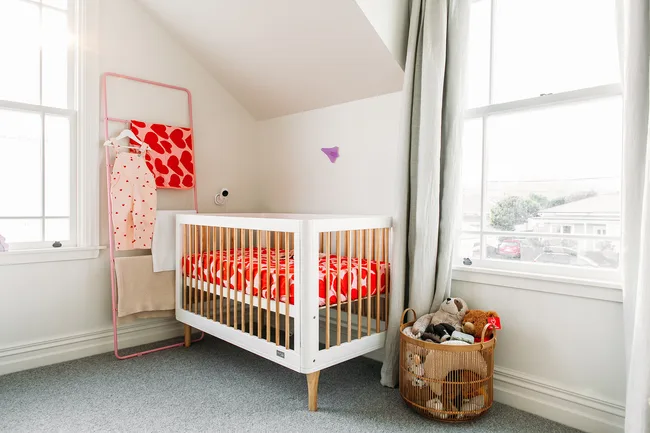 Bright nursery with a white crib, red heart bedding, and a basket of stuffed toys by a sunny window.