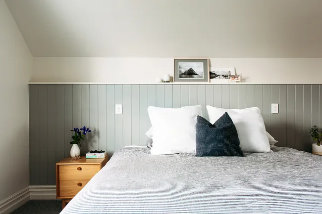 Cozy bedroom with a bed, striped bedding, and decorative pillows. A nightstand with flowers and books beside it.