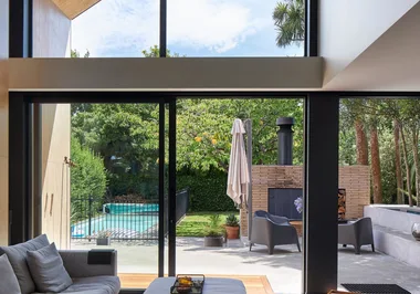 Modern living room view with large glass doors opening to a backyard patio, pool, and lush greenery.