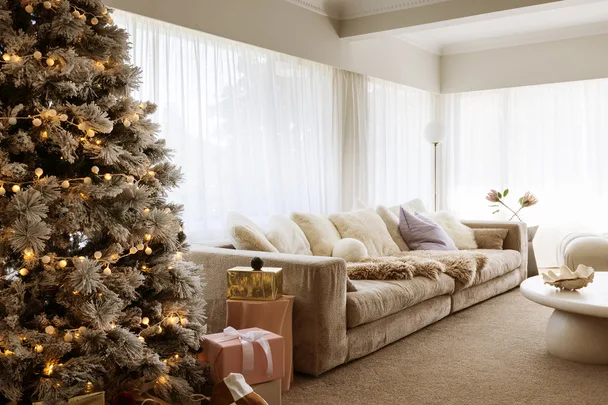 Cozy living room with a decorated Christmas tree, lit with lights, next to a sofa and wrapped gifts.
