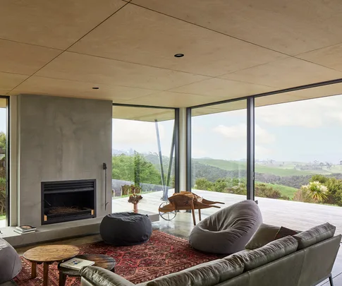 Modern living room with large windows, lush landscape view, cozy seating, rustic coffee table, and a fireplace.