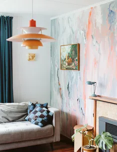 Stylish living room with mid-century lamp, abstract wall, gray sofa, geometric cushions, and framed painting.