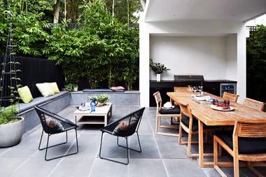Outdoor patio with dining table, chairs, bench with cushions, plants, and a grill under a white pergola.