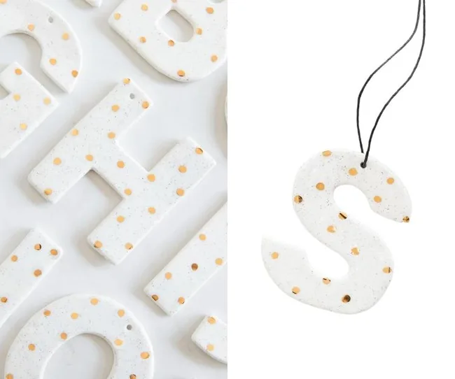 White ceramic letters with gold dots, focusing on an "S" hanging by a black string.