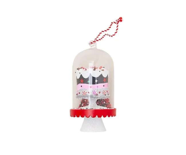 A Christmas ornament shaped like a decorated cake under a clear dome with red accents and a string for hanging.