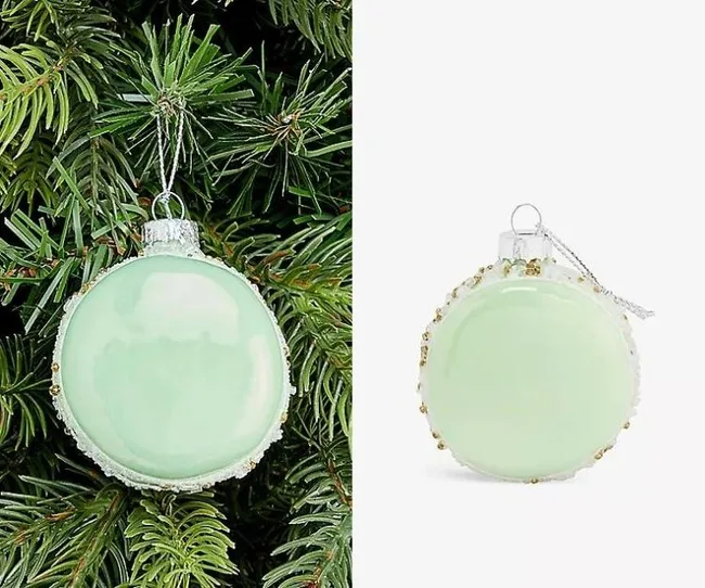 Light green glass Christmas ornament hanging on a pine tree with gold accents, shown from two angles.