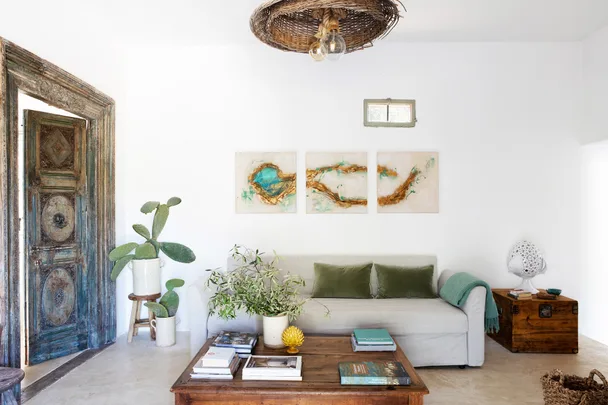 Living room with beige sofa, green cushions, wooden coffee table, cactus plants, wooden door, and abstract wall art.