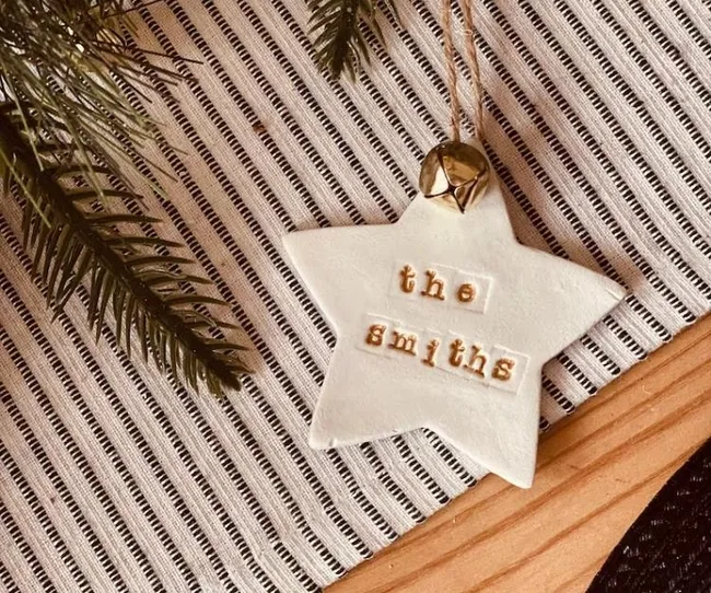 Star-shaped ornament labeled "the Smiths" on striped fabric with pine branches and a jingle bell.