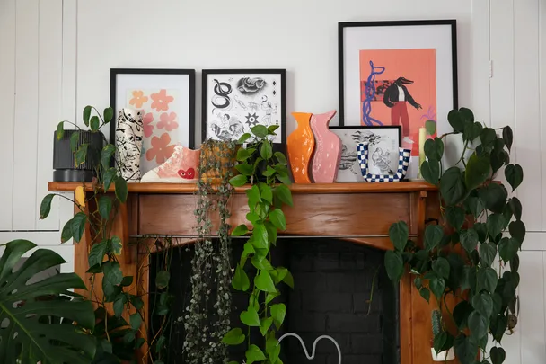 Decorated wooden mantel with framed art, colorful vases, and lush green plants.