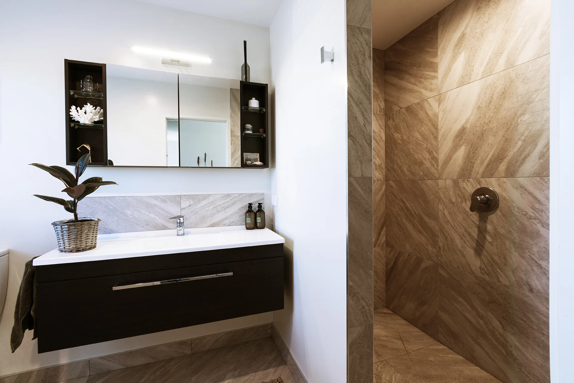 Modern bathroom with a wall-mounted sink, large mirror, and tiled shower area.
