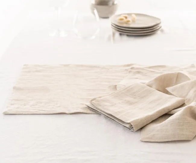 Folded linen napkins on a white tablecloth with stacked plates and blurred background elements.