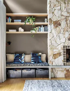 Cozy reading nook with pillows, bookshelves, and stone fireplace in a rustic room.