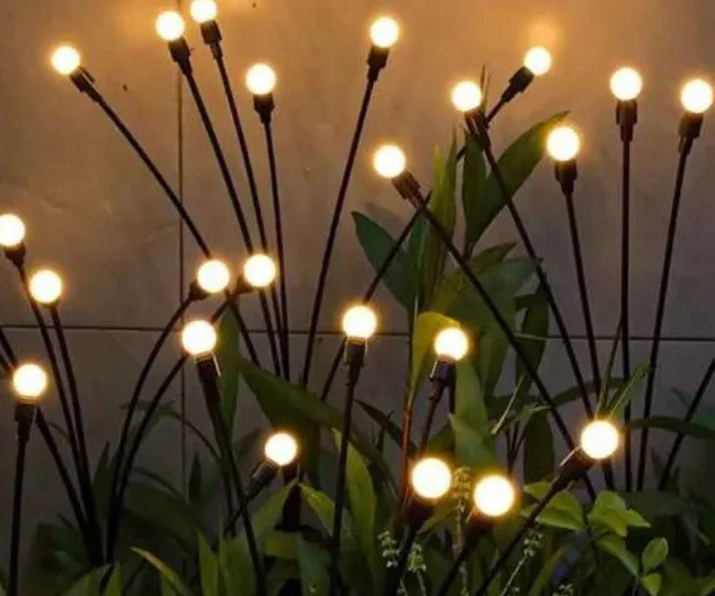 Warm glowing bulbs on tall black stems among green leaves, creating a decorative, artistic light display.