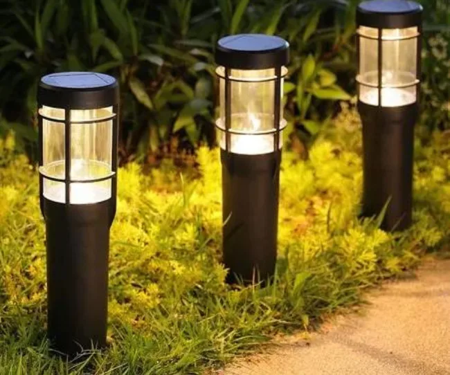 Three solar garden lights illuminate a path, surrounded by greenery.