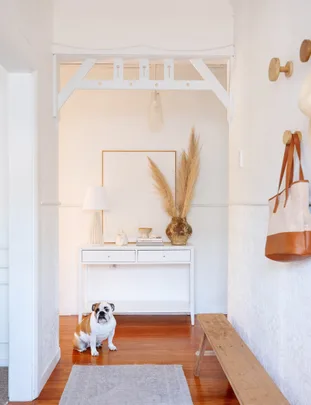A cozy entryway with a cute bulldog sitting on a wooden floor, next to a white console table and decorative items.