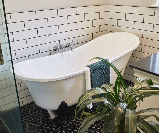 Freestanding white bathtub with towel, surrounded by white subway tiles and black hexagonal floor tiles.
