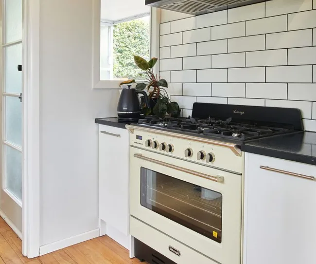 A modern kitchen with a white vintage-style stove, black kettle, plant, and subway tile backsplash.