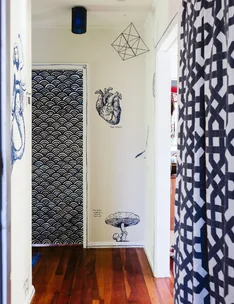 Hallway with wooden floor, wall art of a heart and mushroom, geometric pendant, and patterned curtains and door.