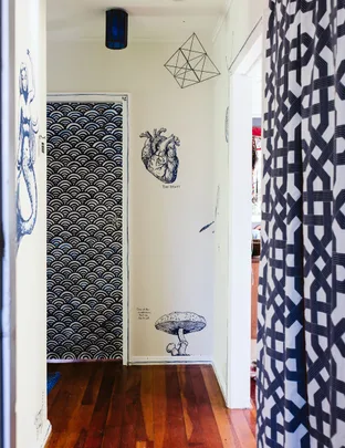 Hallway with wooden floor, wall art of a heart and mushroom, geometric pendant, and patterned curtains and door.