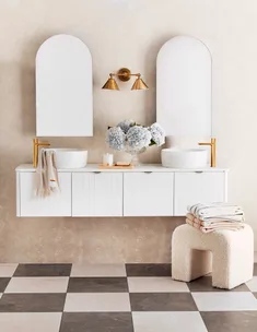 Elegant bathroom with dual sinks, arched mirrors, gold fixtures, hydrangeas in vase, and checkered floor tiles.
