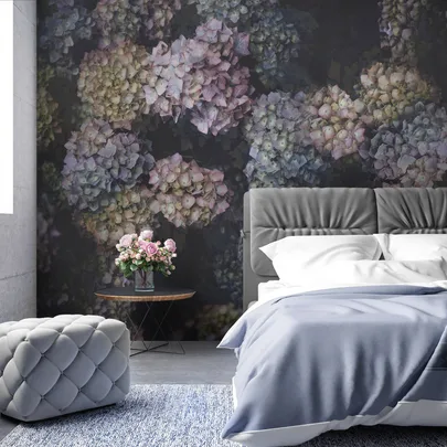 Bedroom with floral wallpaper, gray bed, blue bedding, gray ottoman, and table with pink roses in a vase.