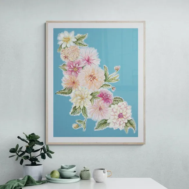 Framed floral painting with pink and white flowers against a blue background, hanging on a green wall above a table.