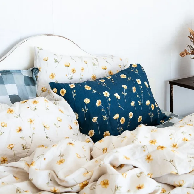 Floral bedding with blue and white pillows featuring yellow flowers on a white wooden headboard.