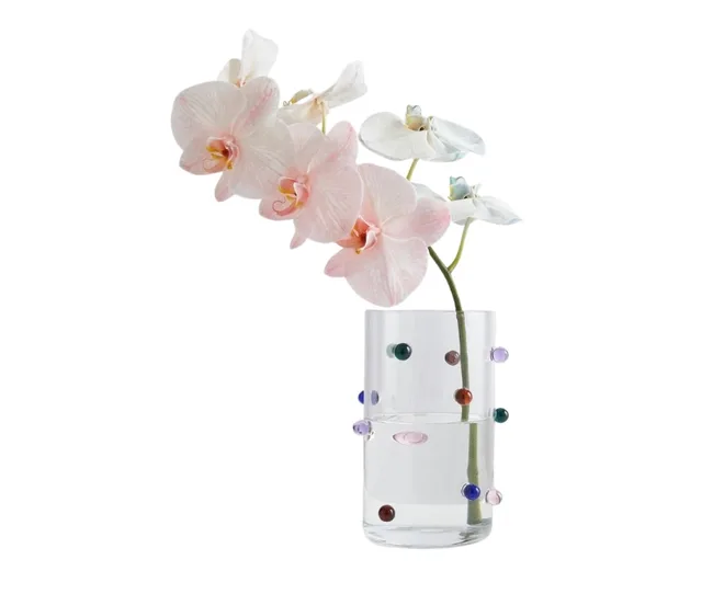 A clear glass vase with colorful orbs holds light pink orchids on long stems, set against a plain background.
