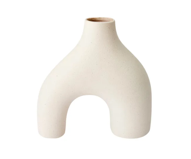 Minimalist sculptural beige ceramic vase with a unique arch-shaped design against a white background.