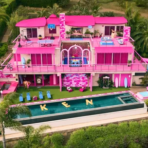 A vibrant pink-themed Barbie Dreamhouse with pool floats spelling "KEN" in the pool.