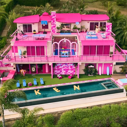 A vibrant pink-themed Barbie Dreamhouse with pool floats spelling "KEN" in the pool.