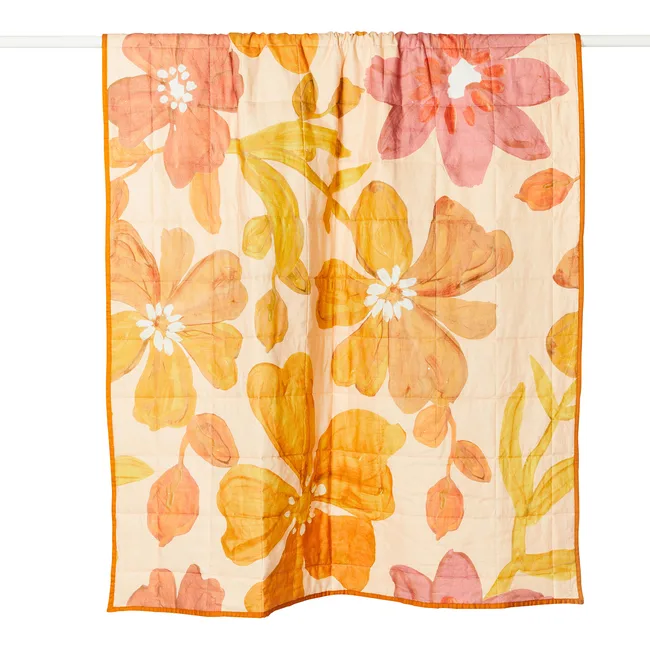A floral-patterned quilt with large orange and pink flowers on a light background hanging on a white rod.