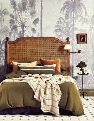 Cozy bedroom with rattan headboard, tropical wallpaper, and earth-toned bedding. Small bedside table with decor.