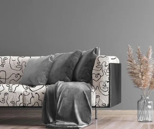 Gray sofa with abstract pattern, gray pillows and blanket; decorative pampas grass in vase on wooden floor.