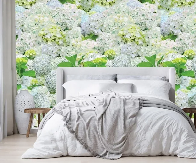 White bed with gray blanket against a floral wallpaper featuring hydrangeas in soft pastel shades.
