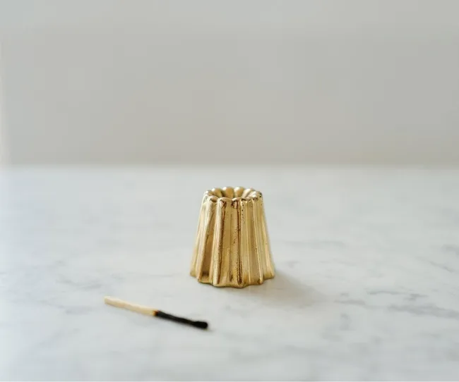 Gold Canel&eacute; baking mold on marble surface with a spent matchstick beside it.