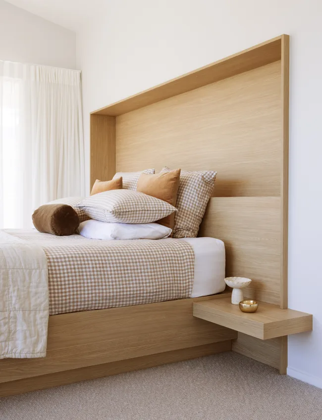 Bedroom with a wooden headboard, checkered bedding, and decorative pillows in warm tones. Simple nightstand with decor.