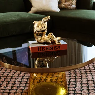 Golden sculpture on Hermès book atop a glass table, with a green sofa in the background.